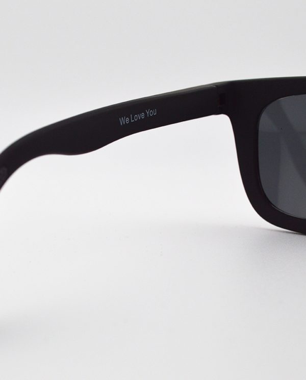 Close-up of black RKT Brodie sunglasses; "We Love You" inscribed on arm.