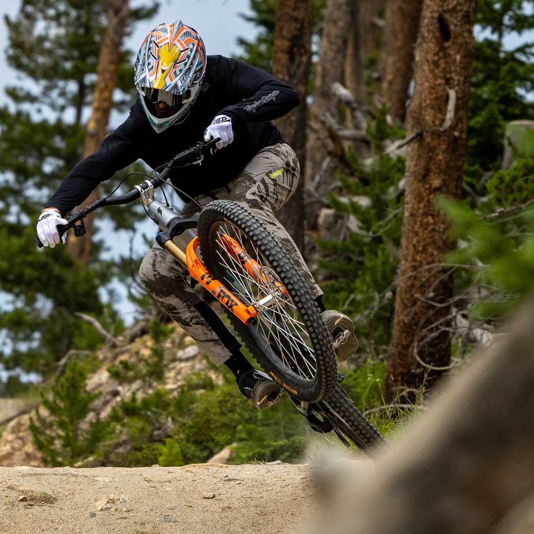 Mountain biker mid-air on a downhill bike jump, showcasing bike's orange suspension.
