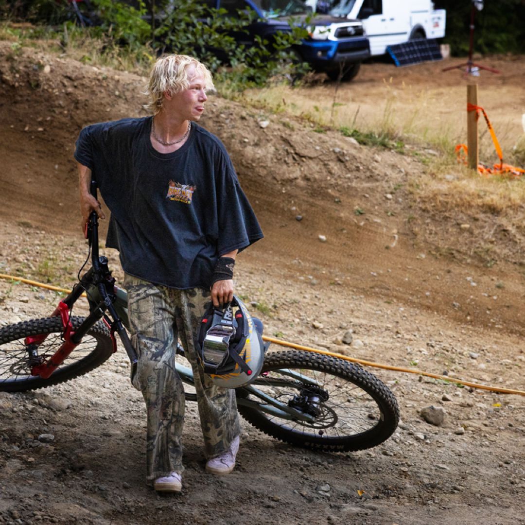 Young male mountain biker carrying his bike and helmet on a dirt trail.