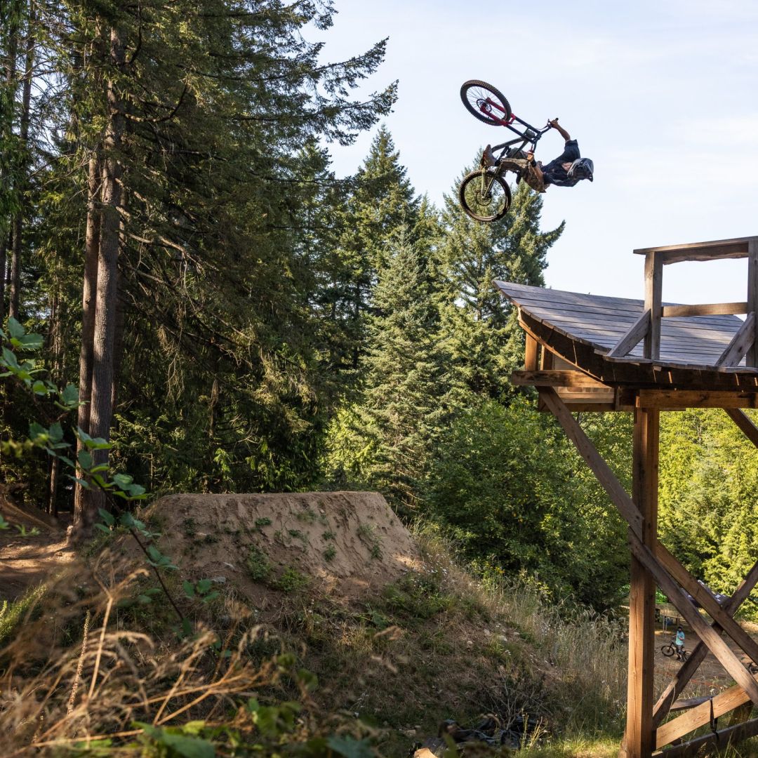 Mountain biker performing a jump off a wooden ramp in a forest